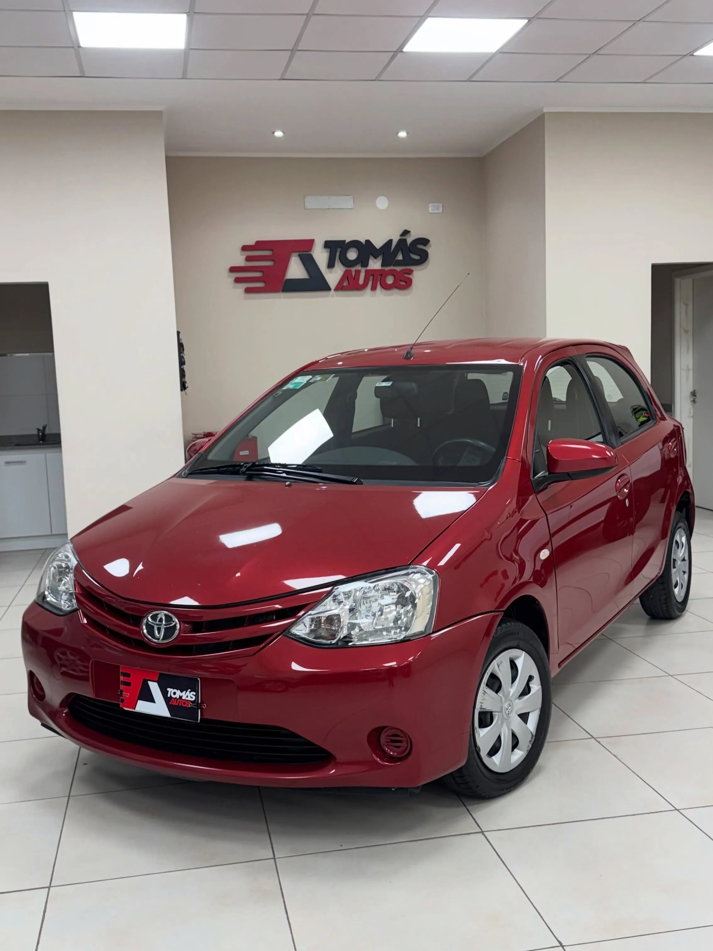 Toyota Etios X 2017 rojo, de frente y perfil izquierdo, en el showroom de Tomás Autos
