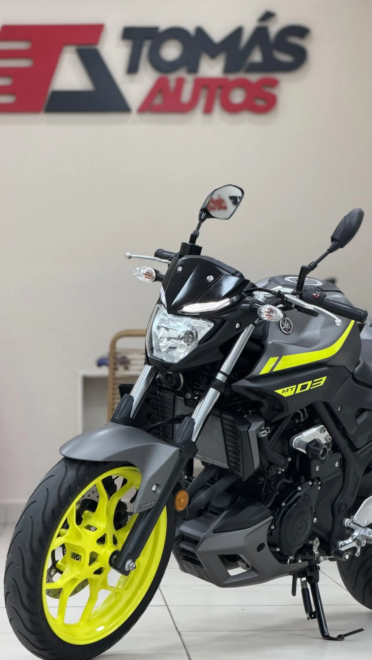 Moto Yamaha MT-03 2020 gris y amarilla, de frente y perfil derecho, en el showroom de Tomás Autos